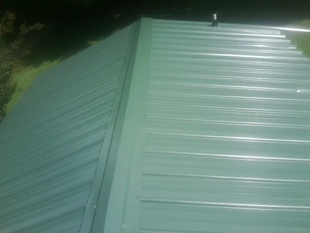 New green metal panels meeting at the ridge of a roof — Flat Roof Repair work by our crew in Riverton