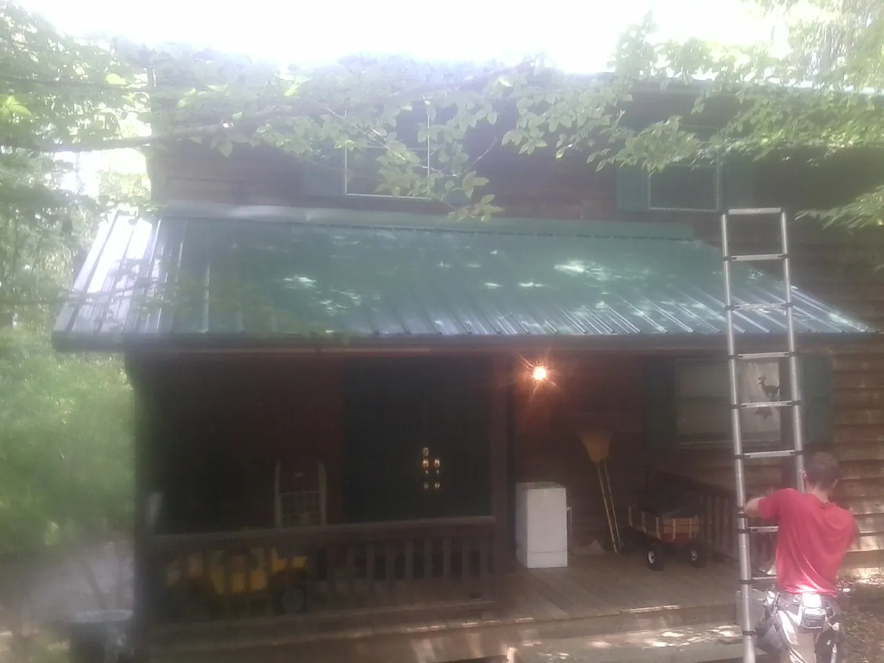 Worker on a ladder at the green porch roof of a wooded cabin in Riverton