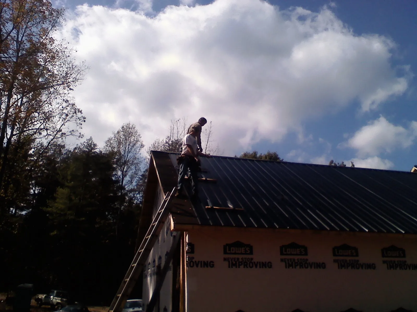 Roofer fastening dark metal panels high against a cloudy sky, from a Roof Inspection job in Riverton